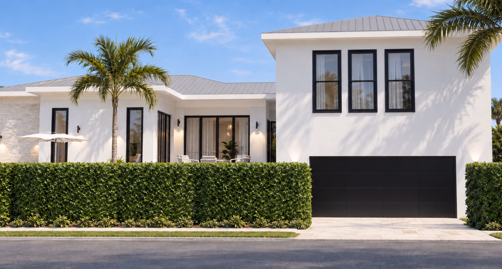 Street view of a white home with a clipped hedge, a black garage door under a two-story wing, and a palm in the front yard.