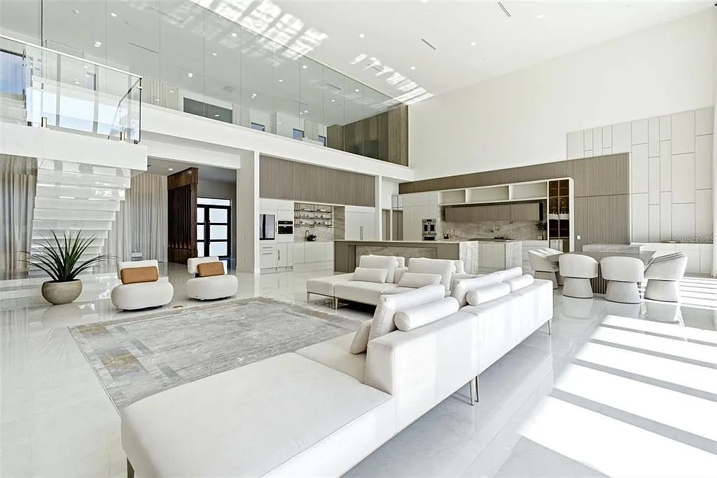 Double-height great room with a glass-railed loft, white sectional sofas, and an open kitchen with stone islands.