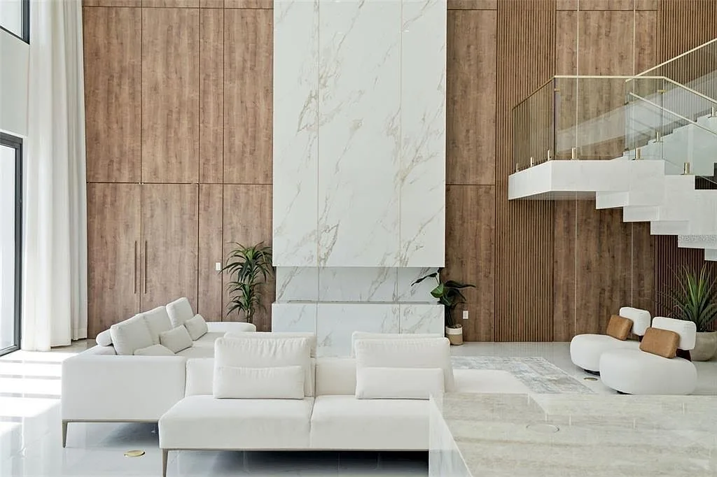 Living room with a book-matched marble fireplace wall between wood panels and a floating white staircase with glass railings.