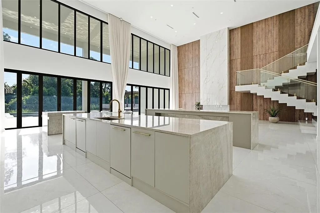 Kitchen island with a stone top and brass faucet, with a floating staircase and wood-paneled wall behind it.
