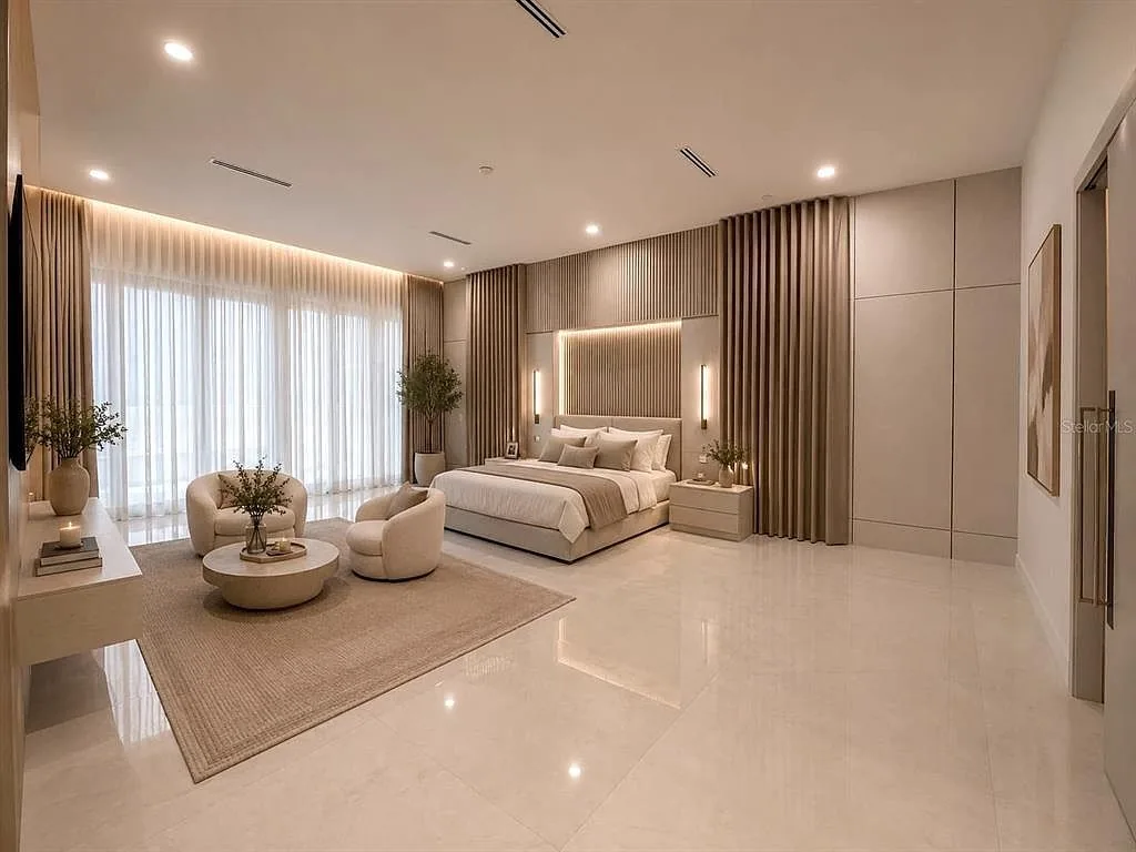 Primary bedroom with a fluted headboard wall, floor-length drapes, and bouclé lounge chairs around a round coffee table.