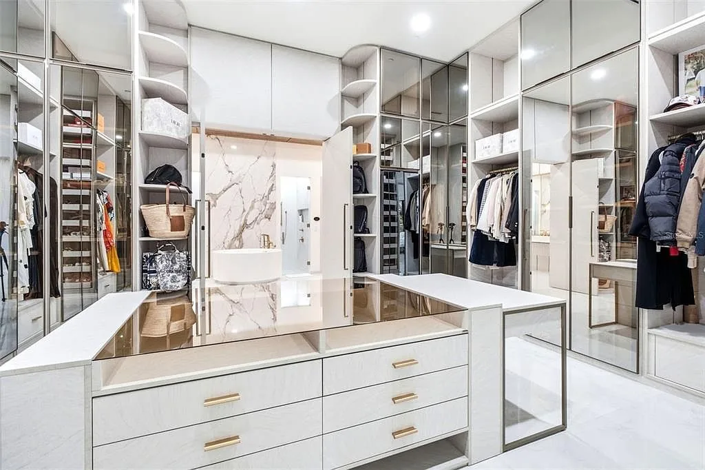 Walk-in closet with glass-front cabinetry, a center island with brass pulls, and a view through to a marble-walled bath.