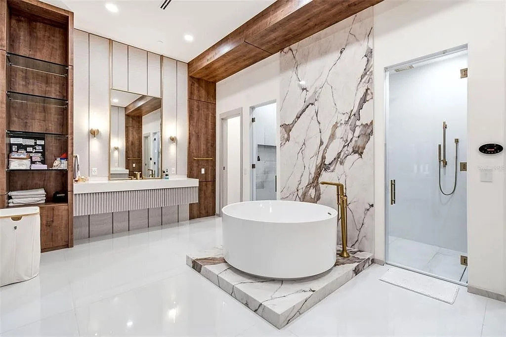 Primary bathroom with a round freestanding tub on a marble platform, a floating vanity, and a glass steam shower.