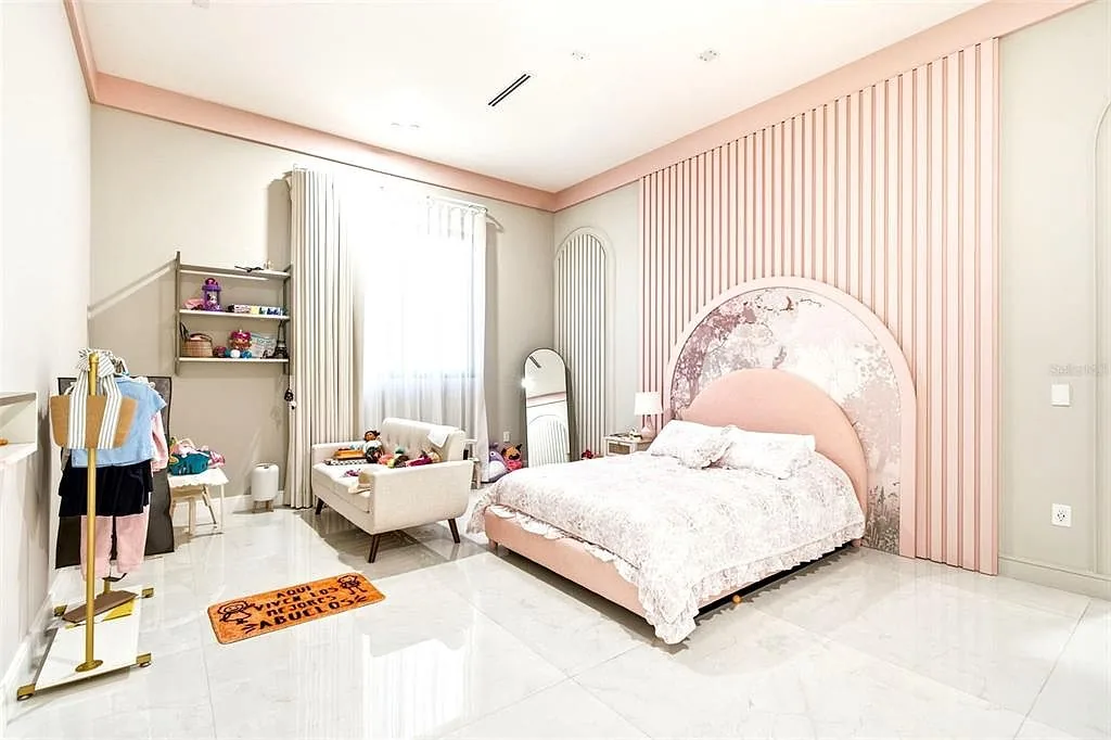Child's bedroom with a pink fluted wall, an arched mural headboard, and linen drapes.