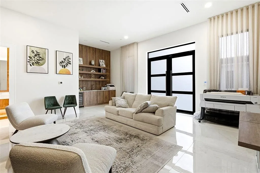 Lounge with a cream sofa, bouclé chairs, and black steel-framed glass doors beside a walnut coffee bar.