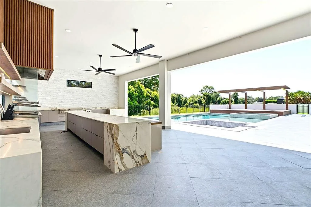 Covered outdoor kitchen with a marble waterfall island, fluted wood cabinetry, and a view of the pool.