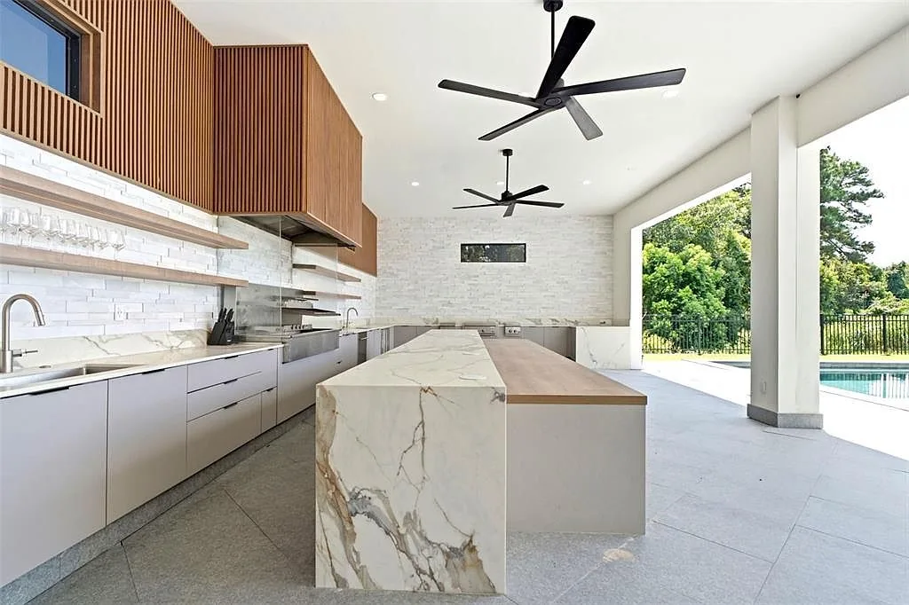 Outdoor kitchen with a marble waterfall island and a wood-top counter under black ceiling fans.