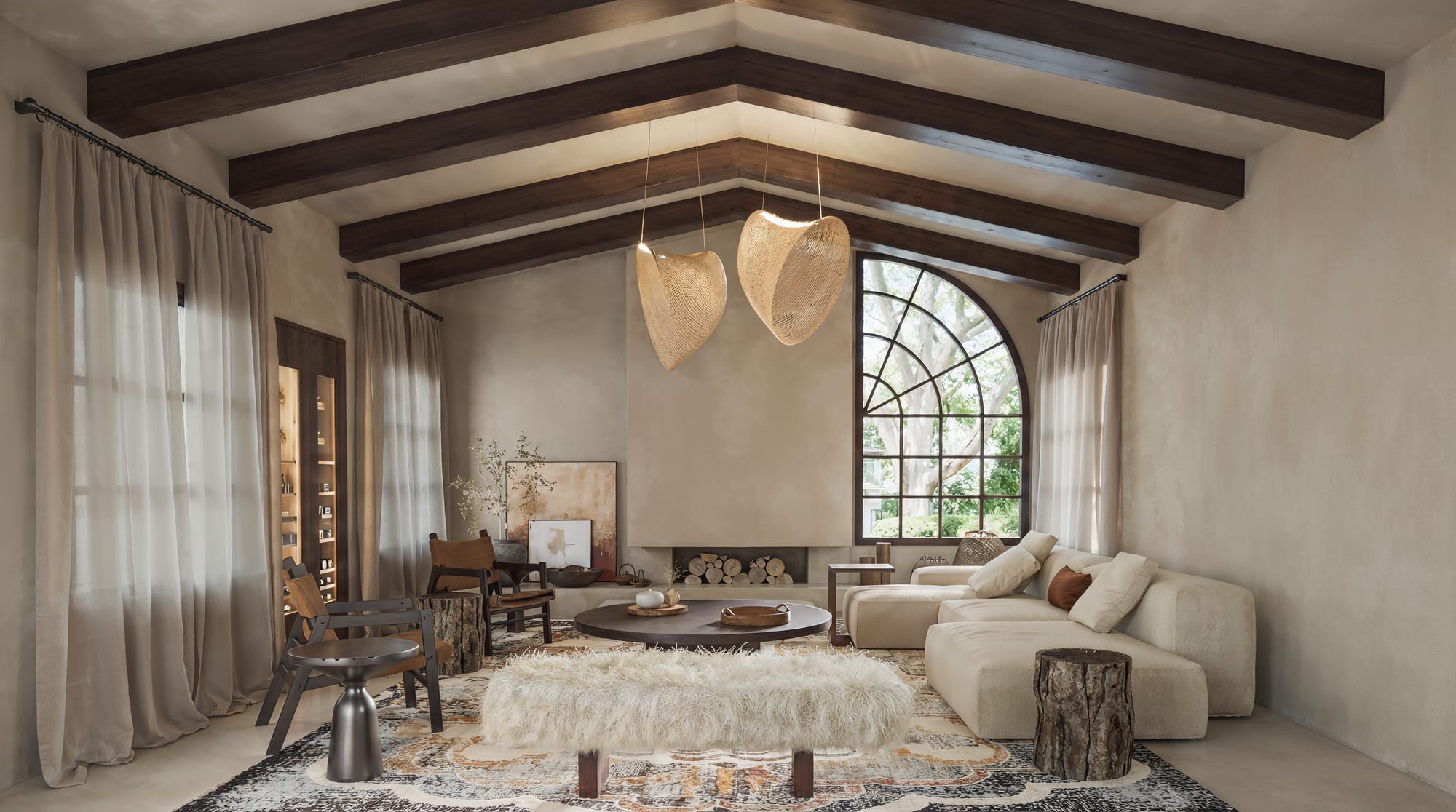 Family room seating area under wood beams, with woven pendants, a patterned rug, and an arched window.