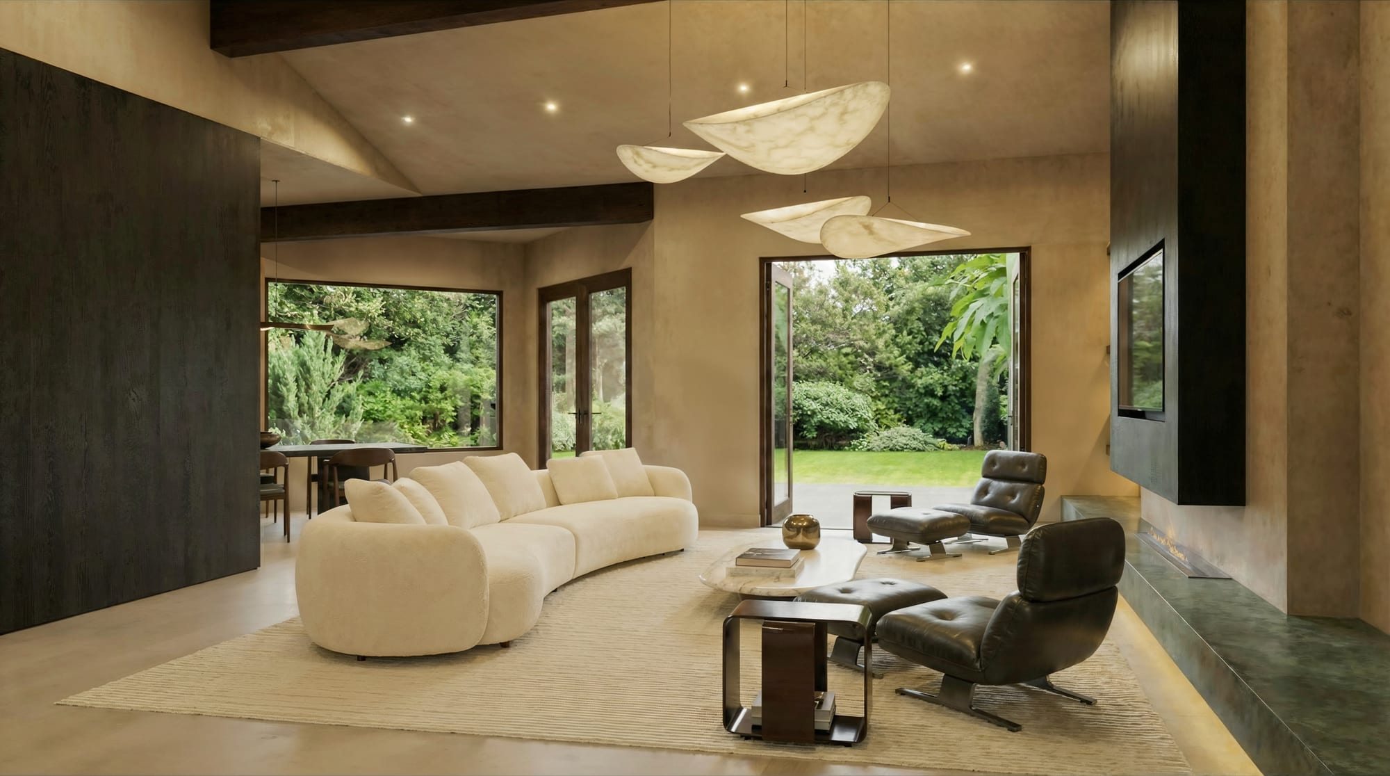 Living room with a curved sofa facing French doors that open to the garden, under floating leaf-shaped pendants.